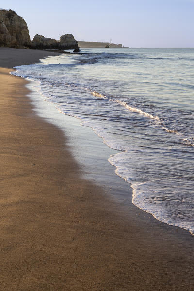 The rising sun illuminates the fine sand bathed by the blue ocean Praia do Vau Portimao Faro district Algarve Portugal Europe