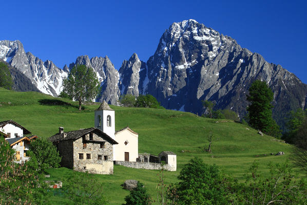 Spring view of the church and the chalets of Dalò with behind the majestic Prata Peak. Valchiavenna. Valtellina. Vallespluga. Lombardy. Italy. Europe.