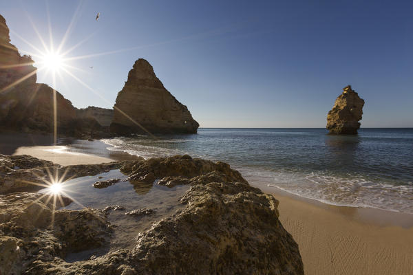 First rays of sun on the cliffs and turquoise water at Praia da Marinha Caramujeira Lagoa Municipality Algarve Portugal Europe