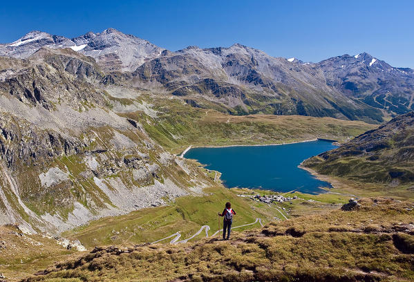 Hikers observe the landscape overlooking the reservoir of Montespluga and on the tops of Valchiavenna. Vallespluga. Lombardy. Italy. Europe.