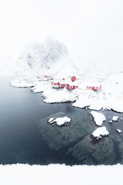 The snowy peaks and frozen sea frame the typical fisherman houses called Rorbu Hamnøy Lofoten Islands Northern Norway Europe