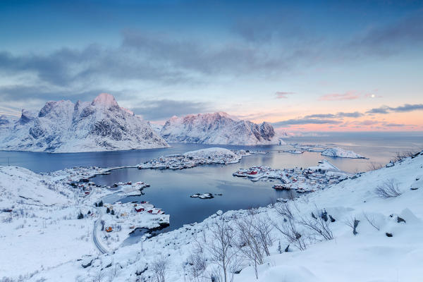 The pink colors of sunset and snowy peaks surround the fishing villages Reine Nordland Lofoten Islands Norway Europe