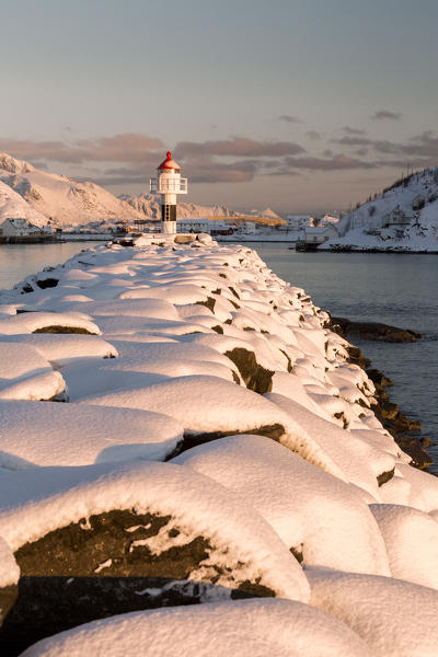 The lighthouse surrounded by snow frames the snowy peaks and the frozen sea Reine Nordland Lofoten Islands Norway Europe