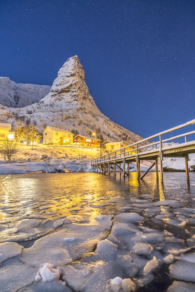 Starry night on the snowy peaks surrounded by the frozen sea Reinevagen Bay Nordland Lofoten Islands Norway Europe