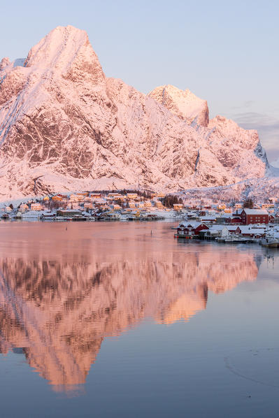 Pink sunrise and snowy peaks frame the  frozen sea and the fishing village Reine Bay Nordland Lofoten Islands Norway Europe