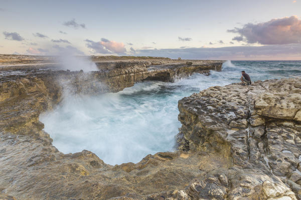 Hiker on the cliffs admires the crashing waves at Devil's Bridge Caribbean Antigua and Barbuda Leeward Islands West Indies