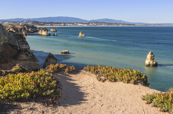 A sandy path toward Praia Dona Ana beach surrounded by turquoise water of the ocean and cliffs Lagos Algarve Portugal Europe