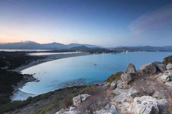 Top view of the bay with sandy beaches and lights of a village at dusk Porto Giunco Villasimius Cagliari Sardinia Italy Europe