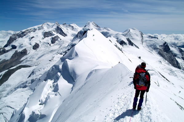 A hiker contemplating the breathtaking view from the Breithorn summit, in the Mount rosa Massif, with the Lyskamm, Castor, Pollux, on the border between Italy and Switzerland Europe