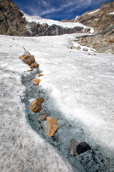 A tiny stream of water making its way towards valley from the glacier Fellaria now melting due to the summer heat, Valmalenco, Valtellina, Lombardy Italy Europe