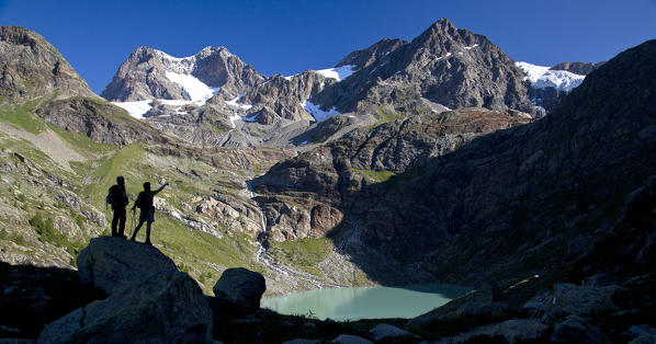 Hikers looking at the glaciers and the peaks of the Bernina Group not far from the Lake of Alp Gera (Lago dell'Alpe Gera), Valmalenco, Valtellina, Lombardy Italy Europe