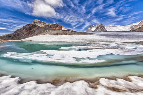 Contrasting harmony: the green water, the white of the ice, the snow and the glacier, the blue sky dotted with unusual clouds are the elements which make the Lake by the Fontana Peak in Valmalenco a memorable place, Valtellina, Lombardy Italy Europe