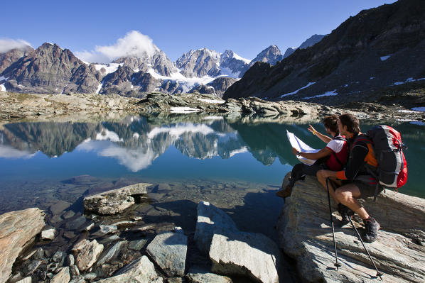 Two hikers admiring the  Bernina group reflecting in the waters of the lake Forbici, Valmalenco, Valtellina, Lombardy Italy Europe