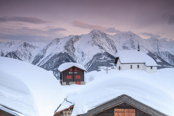 Pink sky at sunset frames the snowy mountain huts and church Bettmeralp district of Raron canton of Valais Switzerland Europe