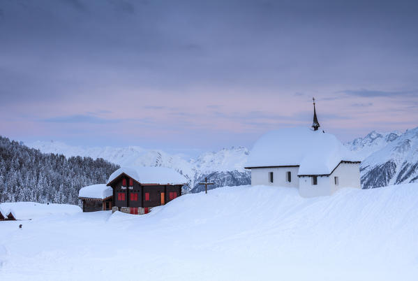 Sunset frames the mountain huts and church covered with snow Bettmeralp district of Raron canton of Valais Switzerland Europe