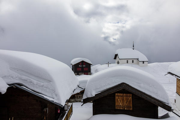 Clouds frame the mountain huts and church covered with snow Bettmeralp district of Raron canton of Valais Switzerland Europe