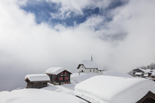 Blue sky and clouds frame the mountain huts covered with snow Bettmeralp district of Raron canton of Valais Switzerland Europe