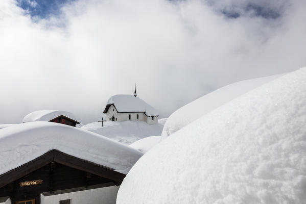 Clouds frame the mountain huts and church covered with snow Bettmeralp district of Raron canton of Valais Switzerland Europe