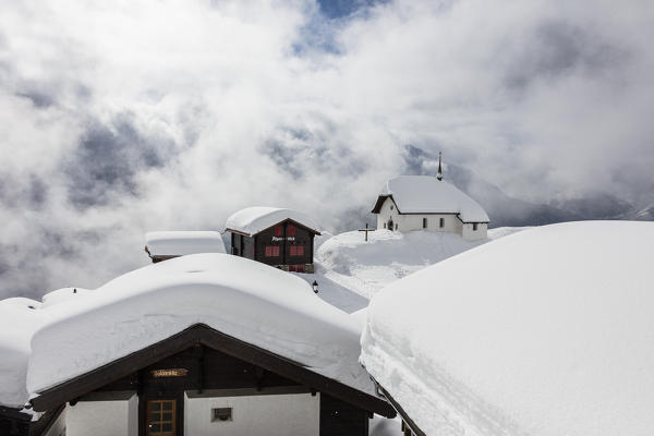 Clouds frame the mountain huts and church covered with snow Bettmeralp district of Raron canton of Valais Switzerland Europe