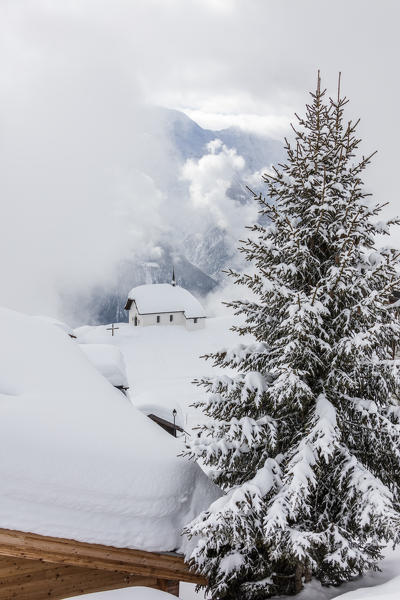 Tree covered with snow frames the alpine church Bettmeralp district of Raron canton of Valais Switzerland Europe