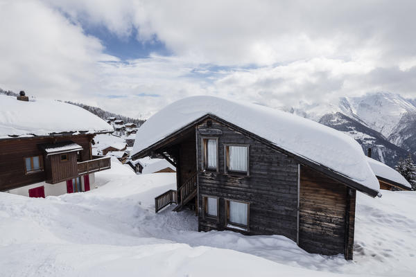 Clouds and blue sky frame the mountain huts covered with snow Bettmeralp district of Raron canton of Valais Switzerland Europe