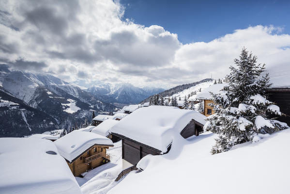 Clouds and blue sky frame the mountain huts covered with snow Bettmeralp district of Raron canton of Valais Switzerland Europe