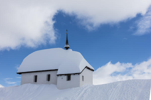 Blue sky and clouds frame the alpine church immersed in snow Bettmeralp district of Raron canton of Valais Switzerland Europe