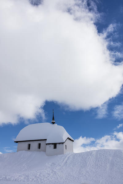 Blue sky and clouds frame the alpine church immersed in snow Bettmeralp district of Raron canton of Valais Switzerland Europe
