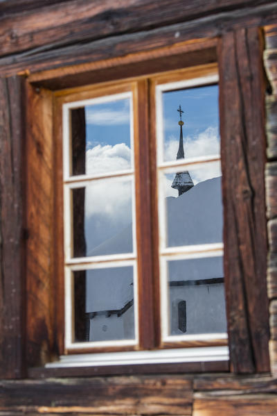 Church covered with snow reflected by window of the wooden hut Bettmeralp district of Raron canton of Valais Switzerland Europe