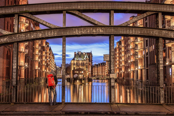 A tourist admires water castle and buildings reflected in the canal at dusk Poggenmühlenbrücke Altstadt Hamburg Germany Europe