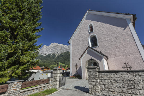 Typical church of alpine village surrounded by peaks and woods Garmisch Partenkirchen Oberbayern region Bavaria Germany Europe