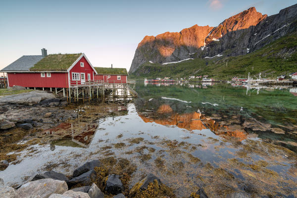 Fishing village and peaks reflected in water under midnight sun Reine Nordland county Lofoten Islands Northern Norway Europe