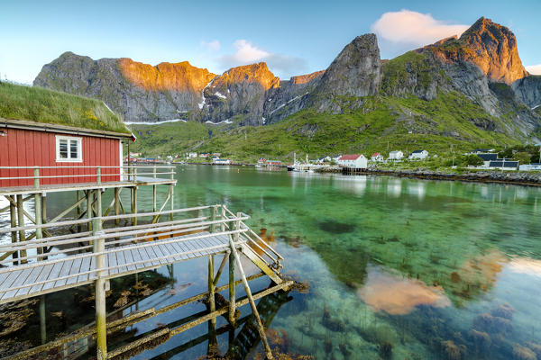 Midnight sun on fishing village and peaks surrounded by clear sea Reine Nordland county Lofoten Islands Northern Norway Europe