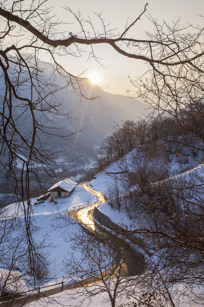 Sun on the alpine road framed by woods Soglio canton of Graubünden Maloja District Bregaglia Valley Engadine Switzerland Europe