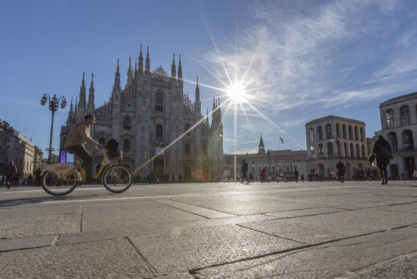 Cyclist under a warm spring sun in front of the facade of the Gothic Duomo Milan Lombardy Italy Europe
