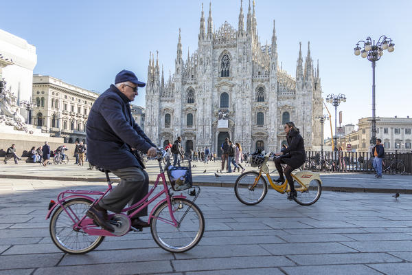 Cyclists under a warm spring sun in front of the facade of the Gothic Duomo Milan Lombardy Italy Europe