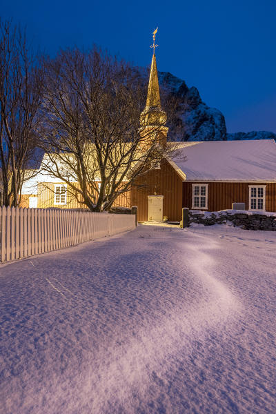 Lights on the typical wooden church surrounded by snow Flakstad Lofoten Islands Northern Norway Europe