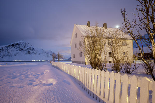 Full moon and lights on the typical wooden house surrounded by snow Flakstad Lofoten Islands Northern Norway Europe