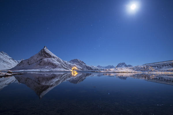 Full moon and stars light up the snow capped peaks reflected in sea Volanstinden Fredvang Lofoten Islands Northern Norway Europe