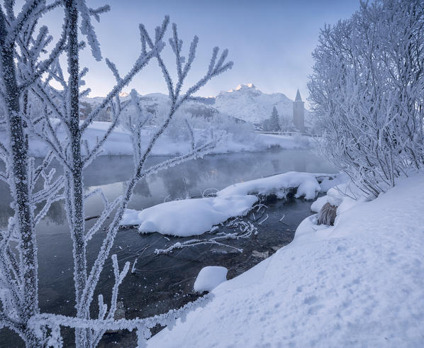 The frost and snow on tree branches frame the river Inn at dawn Sils Canton of Graubunden Engadine Switzerland Europe