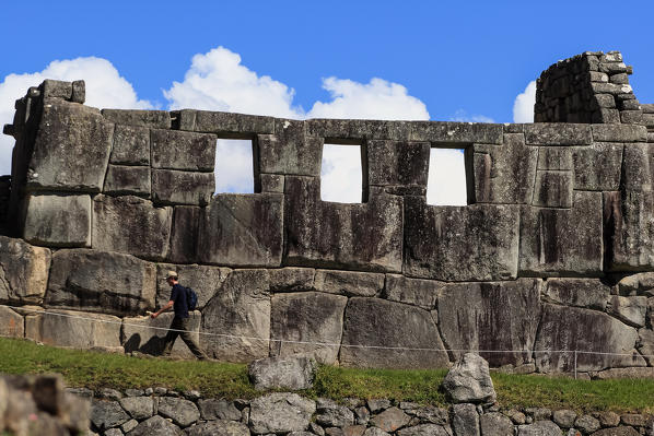 A tourist walking around the Inca ruins of Machu Picchu by the Temple of the Three Windows, consisting of only three walls on a rectangular base and covered by a roof made of adobe walls constructed from large blocks of solid rock carved in polygonal shape forming a conglomerate of perfectly matched stones each other, leaving space for, originally five windows, although there are today only three of them indicating the exact location of the sunrise Peru South America