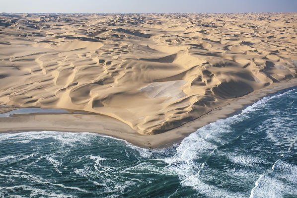 Aerial shot of the cold waters of the Atlantic Ocean meeting the sand dunes of the Namib Desert. Namibia. Africa
