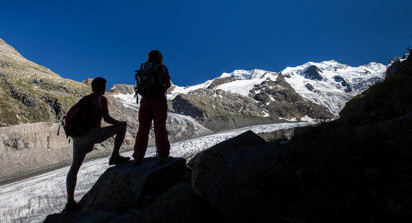 On their way back in the Valley of Morteratsch, some hikers are enjoying the last lights on the Bernina glaciers, Engadin, Switzerland Europe