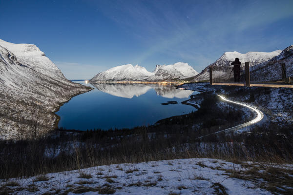 Photographer on platform admires the snowy peaks reflected in sea Bergsbotn Senja Troms County Norway Europe