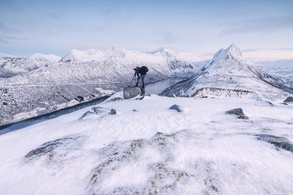 Photographer on snowy peak admires the frozen sea framed by soft lights of dusk Gryllefjorden Senja Troms County Norway Europe