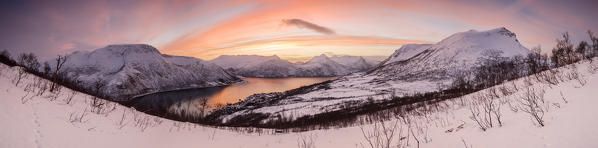 Panorama of frozen sea surrounded by snow  framed by the orange clouds at sunset Gryllefjorden Senja Troms County Norway Europe