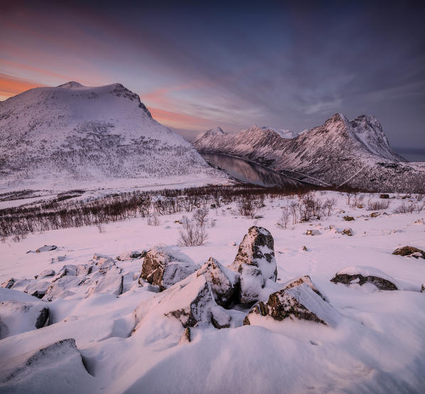 Panorama of snowy peaks surrounded by frozen sea under orange clouds at sunset Gryllefjorden Senja Troms County Norway Europe