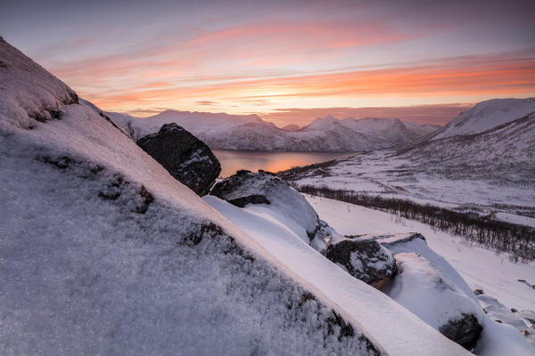 The frozen sea surrounded by snow framed by orange clouds at sunset Torsken Senja Troms County Norway Europe