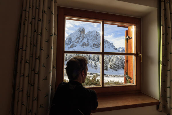 A man admires Sass De Putia surrounded by snow from the glass of a window Passo Delle Erbe Funes Valley South Tyrol Italy Europe