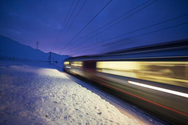 Bernina Express train runs fast in the snowy landscape at dusk Bernina Pass Canton of  Graubünden Engadine Switzerland Europe
